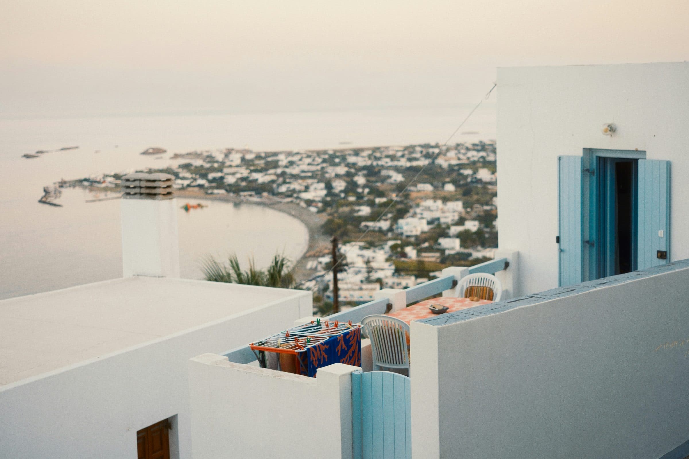 A whitewashed island house with blue shutters above a bay at dusk